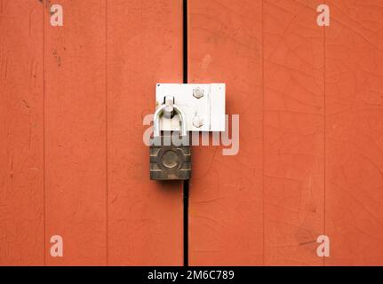 Ein Metallvorhängeschloss, das zwei Holztüren im Freien verriegelt Stockfoto