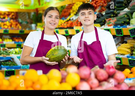 Positiv lächelnde Verkäuferin und Verkäufer in der Schürze, die frisches Obst im Geschäft anbietet Stockfoto