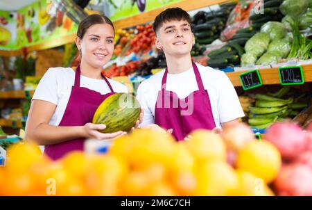 Positiv lächelnde Verkäuferin und Verkäufer in der Schürze, die frisches Obst im Geschäft anbietet Stockfoto