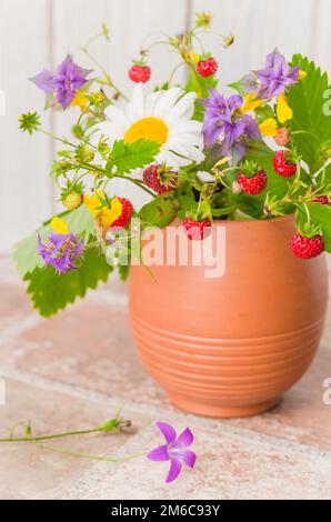 Reife Erdbeeren und einen Blumenstrauß der Wald Blumen in einem Ton Becher Stockfoto