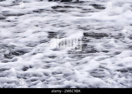 Natürliches Meerwassermuster. Im Winter fließt schaumiges Wasser am Strand. Kleine Wellen mit Whitecaps. Ostsee, Mecklenburg-Vorpommern, Deutschland Stockfoto