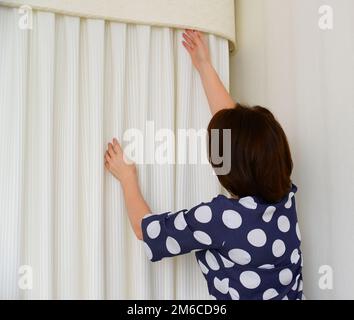 Eine Frau, die weiße Vorhänge am Fenster aufhängt Stockfoto