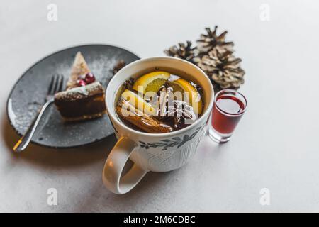 Weihnachtstee mit Zimt, Anis und Orangenscheiben serviert mit Kuchen und Spirituosen. Grauer Tisch. Speicherplatz kopieren. Hochwertiges Foto Stockfoto