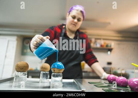 Dekorationsprozess. Eine Frau, die blaue Glasur auf Pralinen gießt. Unkonventionelle Dekorationen auf Kuchen. Hochwertiges Foto Stockfoto