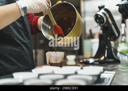 Der Koch bereitet Schokoladenteig in einer Rührschüssel aus Edelstahl mit einem Teigschaber zu. Cupcake-Rezept. Speicherplatz kopieren. Hochwertiges Foto Stockfoto