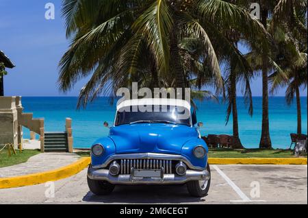 Amerikanisch-blauer Oldtimer unter Palmen am Strand in Varadero Cuba - Serie Cuba R. Stockfoto