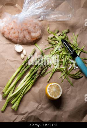 Ein Haufen grün geschälter Spargel mit Zitrone und Garnelen auf dem Tisch Stockfoto