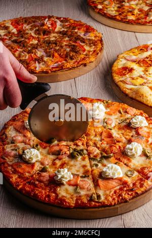 Die Hand eines Mannes schneidet Pizza mit einem Messer Stockfoto