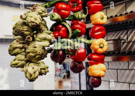 Artischocken und Paprika in verschiedenen Farben hängen in einer Küche Stockfoto