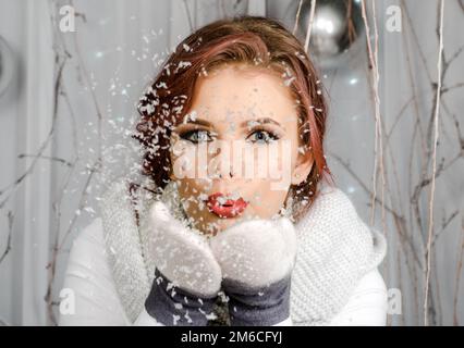 Weihnachten, Weihnachten, Menschen, Glückskonzept - glückliches Mädchen in Winterkleidung, das auf Palmen bläst Stockfoto