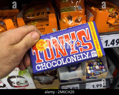 Dortmund, Deutschland - 19. Februar 2022: POV männliche Hand-Halten-Packung mit Tony's Chocolonely Toffee Schokolade mit Regalen im Supermarkt im Hintergrund Stockfoto