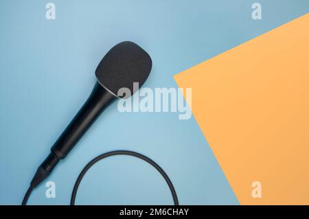 Konzertmikrofon, das über ein Kabel auf blauem Hintergrund mit einem orangefarbenen Pfeil verbunden ist. Karte. Speicherplatz kopieren Stockfoto