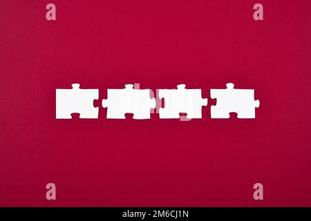Vier weiße Puzzleteile auf einem isolierten roten oder magentafarbenen Hintergrund. Konzept einer vorgefertigten Lösung für eine Frage oder ein Problem. Stockfoto