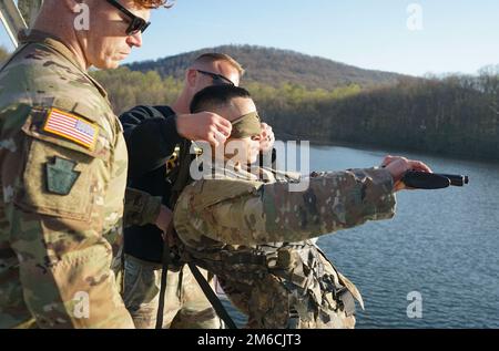 Sgt. 1. Klasse Erich Friedlein, unkommissionierter Offizier, verantwortlich für das Ranger and Sapper Assessment Program der Pennsylvania National Guard, verbunden einem Dienstmitarbeiter während des Kampfwasserüberlebenstests der RSP am 22. April 2022 in Fort Indiantown Gap, Pa Die Mitglieder des Dienstes wurden herausgefordert, einen Kampfladeträger zu tragen, eine Gummiwaffe zu tragen und die Augen verbunden, als sie von einem Pier sprangen und an Land schwimmen mussten Stockfoto