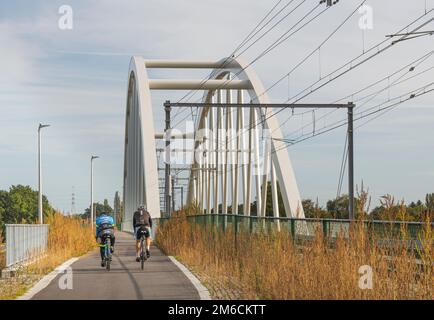 Hasselt. Limburg - Belgien 27-09-2021. Wanderräder im Herbst. Zwei Fahrradfahrer fahren in den Vororten an einer Eisenbahnbrücke vorbei Stockfoto