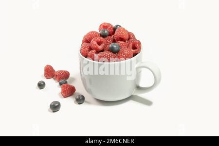 Himbeeren und Heidelbeeren in einem großen grauen Becher auf weißem Hintergrund Stockfoto