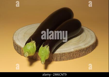 Zwei reife Auberginen auf einem Holzständer auf orangefarbenem Hintergrund. Knapp, rustikal Stockfoto