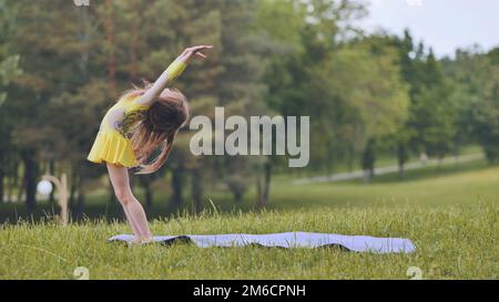Ein kleines Mädchen führt die Elemente der rhythmischen Gymnastik im Park auf. Stockfoto