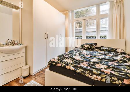 Ein Schlafzimmer mit einem Bett, Kommode und Spiegel an der Wand vor der Tür zum Badezimmerbereich Stockfoto