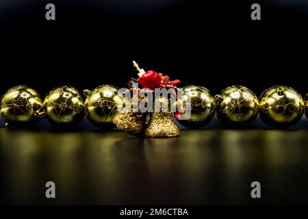 Goldene Weihnachtsbälle und Glocken auf schwarzem Hintergrund. Stockfoto