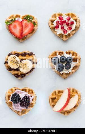 Kleine herzförmige Waffeln mit verschiedenen Aufstrichen und Obst. Stockfoto