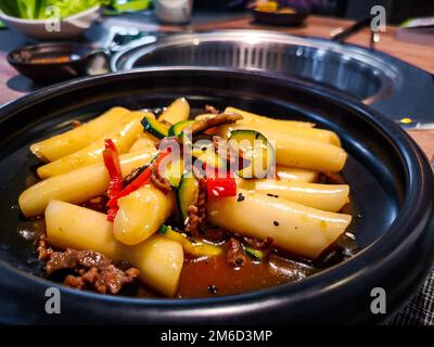 Koreanisches Tteokbokki-Reisklößchen, schwarzes Gericht in einem koreanischen ethnischen Restaurant mit süßem Ganjang-Sojasauce-Fleisch und Zucchini-Glocke Stockfoto