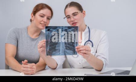 Der Arzt konsultiert eine kaukasische Frau und kommentiert die Röntgenaufnahme der Lunge. Stockfoto