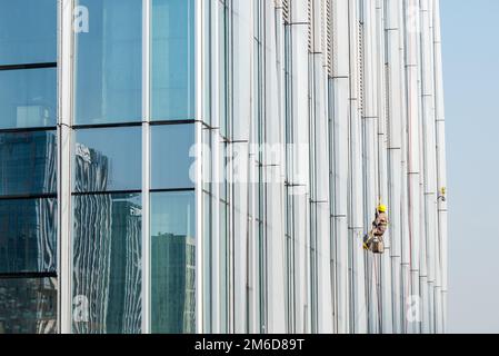 Arbeiter putzt an einem sonnigen Tag die Fassadenfenster des Wolkenkratzers Stockfoto