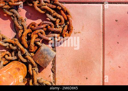 Eine alte rostige Kette und ein Vorhängeschloss, die an einem Pfosten befestigt sind und auf dem Boden liegen. Stockfoto