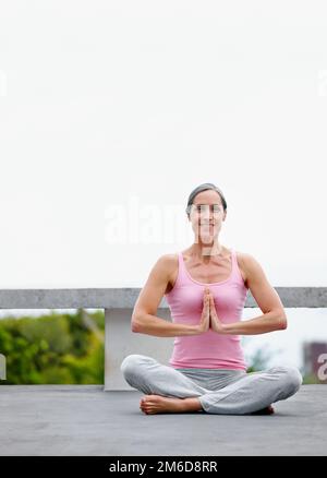 Meditation wirkt Wunder für mich. Eine attraktive reife Frau, die Yoga in Lotusposition praktiziert. Stockfoto