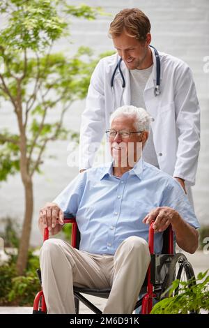 Pflege des allgemeinen Wohlbefindens seiner Patienten. Ein männlicher Arzt schubst seinen älteren Patienten im Rollstuhl nach draußen. Stockfoto