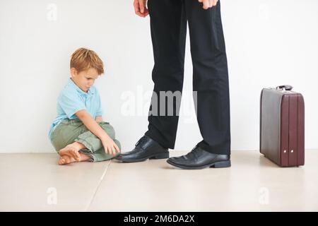 Nein, gehen Sie nicht hin. Ein kleiner Junge auf dem Boden, sehr unglücklich, dass sein Faher zur Arbeit geht. Stockfoto