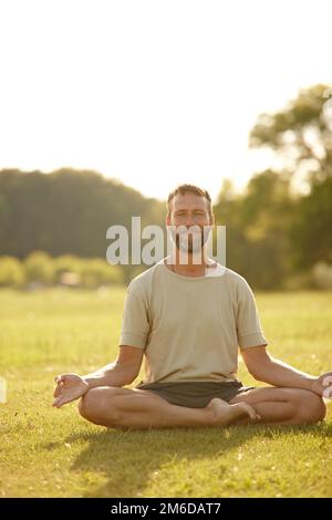 Genießen Sie die Schönheit der Natur beim Yoga. Porträt eines hübschen erwachsenen Mannes, der im Freien Yoga macht. Stockfoto