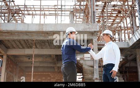 Architekten- und Bauingenieure schütteln sich die Hand, während sie auf einer Baustelle im Freien arbeiten. Stockfoto