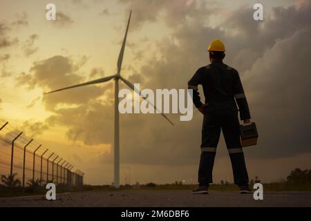 Inspektionsingenieure, die bei Sonnenuntergang eine Windturbine mit Sicherheit im Windpark vorbereiten und deren Fortschritt überprüfen. Stockfoto