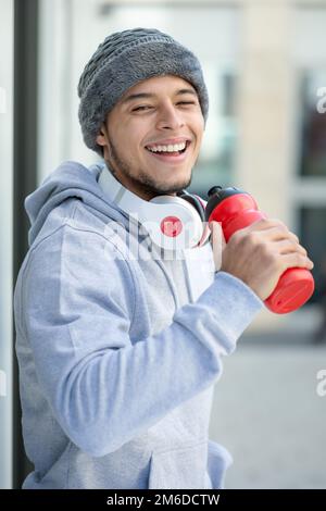 Lächelnder junger latino trinkt Sport im Porträtformat Fitness Winter Stockfoto