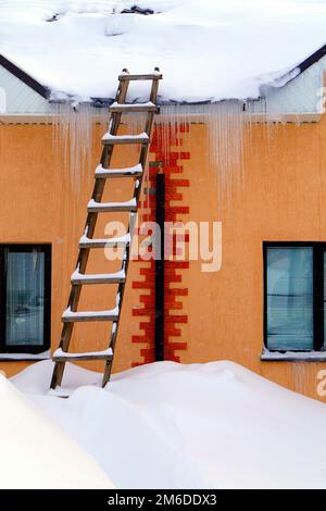 Auf einem Wohnhaus liegt viel Schnee und große Schneeverwehungen. Stockfoto