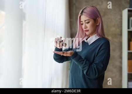 Eine junge Asiatin, die sich zu Hause traurig und einsam fühlt. Frau, die Medizin nimmt Stockfoto