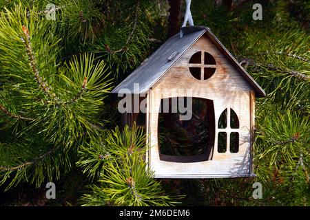 Ein schöner hölzerner Vogelfutterplatz in Form eines Hauses hängt auf einer grünen Fichte. Stockfoto