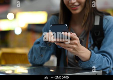 Freigestellte Aufnahme einer Reisenden mit Smartphone, während sie im Street Food Restaurant im Freien sitzt Stockfoto