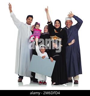 Kultur feiern. Studio-Porträt einer überglücklich muslimischen Familie mit einem leeren Schild isoliert auf weiß. Stockfoto