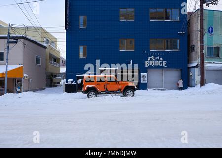 Hokkaido, Japan - 19. Dezember 2022 : In der schneebedeckten Straße in Hokkaido Steht Ein stilvoller orangefarbener Jeep Stockfoto