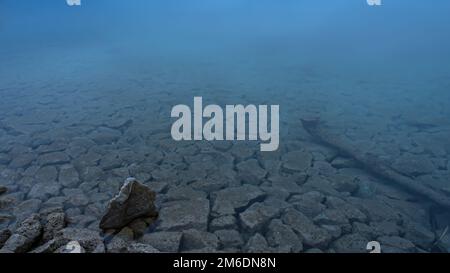 Klares Wasser mit Felsen am Ufer eines blauen Sees im Winter Stockfoto