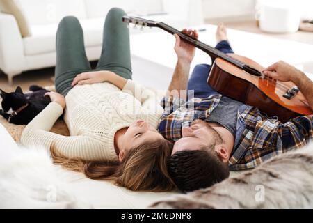 Es ist ein Lied über Liebe und Katzen. Ein junger Mann, der Gitarre spielt, während er mit seiner Freundin auf dem Boden liegt. Stockfoto