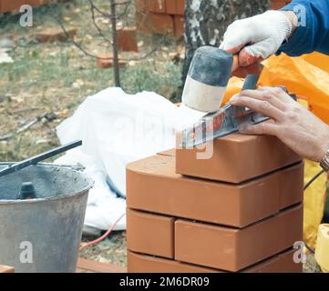 Ein Mann baut eine Mauer. Brick hat die Lösung aufgetragen. Bau eines Ziegelhauses. Stockfoto