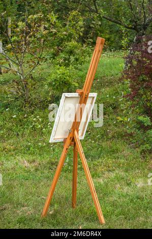 Faltbare Holzstativ-Staffelei mit Leinwandrahmen für die Bemalung auf grünem Gras Sommergarten Stockfoto