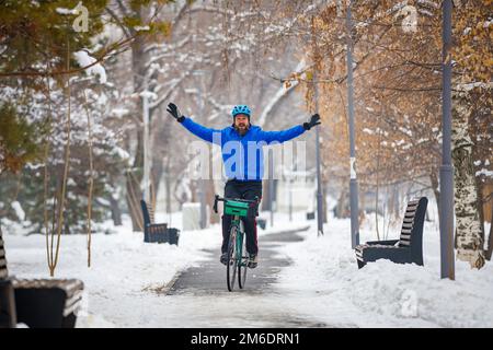Ein bärtiger Mann fährt Fahrrad, ohne das Lenkrad zu halten. Radfahren im Winterpark. Aktive Winteraktivitäten Stockfoto