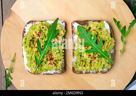 Sandwiches zum Frühstück - Scheibe Vollkornbrot, Frischkäse, Guakomole, garniert mit Rucola, Paprika auf Holztisch Top View Flat Lay gesundes Food Konzept hausgemacht Stockfoto