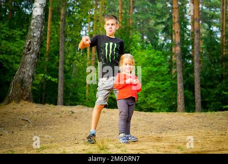 Ein Junge und ein Mädchen tanzen fröhlich auf einer Lichtung im Wald. Stockfoto