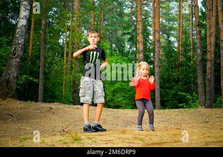 Ein Junge und ein Mädchen tanzen fröhlich auf einer Lichtung im Wald. Stockfoto